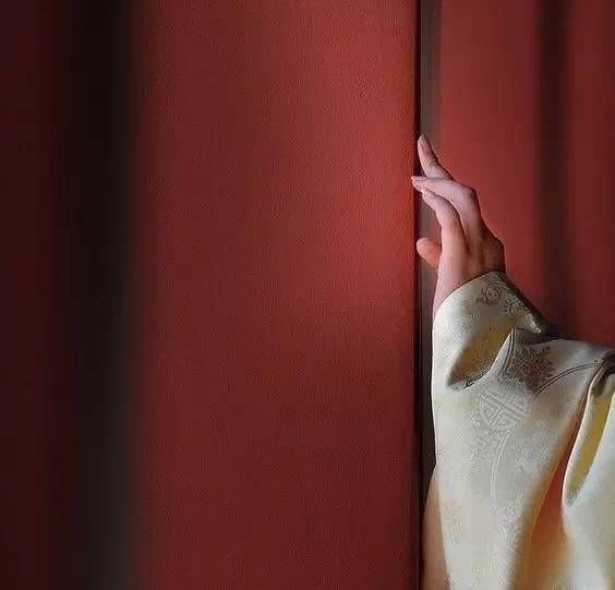 A hand reaching through a red curtain — the quiet intimacy of returning home for postpartum care